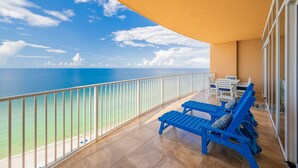 A balcony with a view of the sea, blue lounge chairs, and a table with chairs. - Phoenix Gulf Shores 1602-2 2 Bedroom Condo (Gulf Shores)