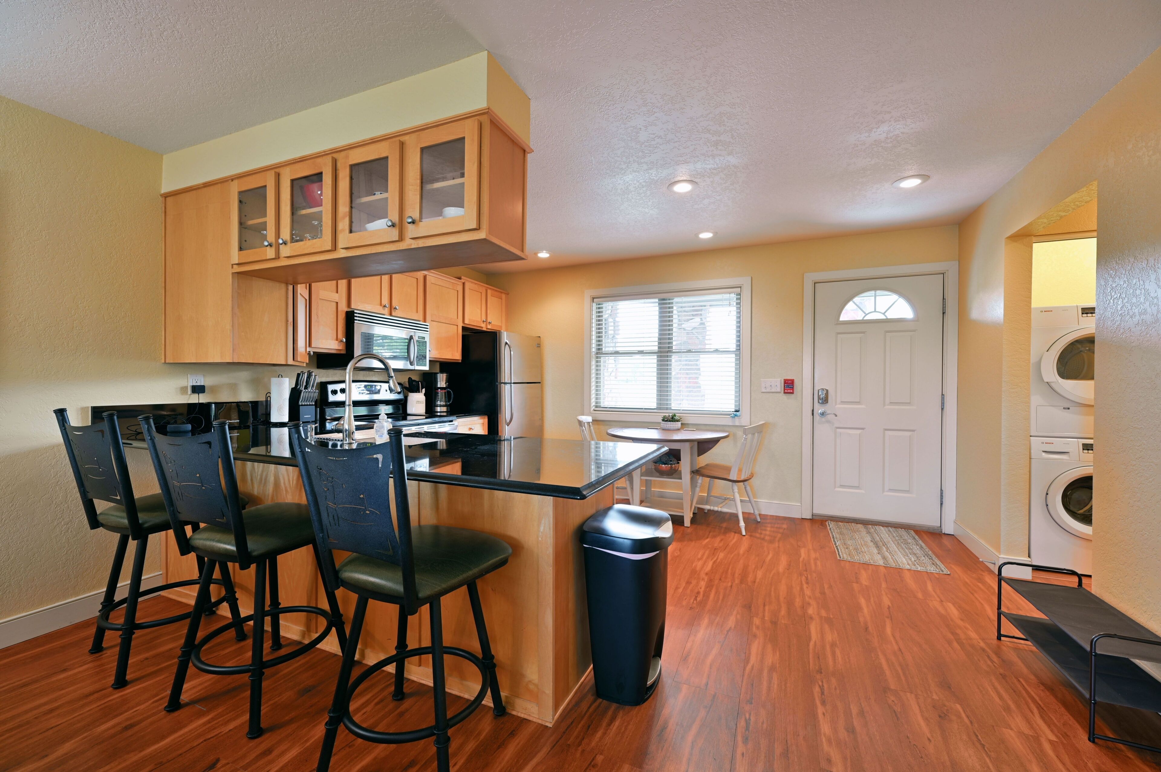 A compact kitchen with wooden cabinets, a central island with bar stools, a microwave, and a refrigerator.