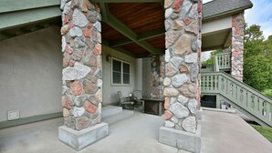 A covered patio area with stone pillars, a wooden ceiling, and a staircase leading to a second level. - Unit 109 2 Bdrm/ 2 Ba 2 Bedroom Condo by RedAwning (Birchwood)