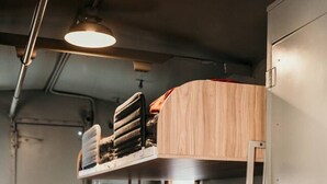 Un lit superposé avec une tête de lit en bois, une fenêtre et une échelle en métal.