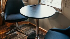 Une pièce de taille modeste, avec une table ronde et deux chaises, un téléviseur fixé au mur et une fenêtre donnant sur l’extérieur.