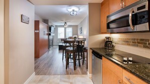 A modern kitchen with wooden cabinets, a stainless steel microwave, and a dining area with a table and chairs.