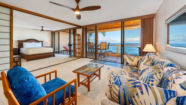 A spacious room with a bed, a sofa, a coffee table, and a balcony with a view of the ocean.