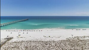 A beach with a long pier extending into the ocean, sandy beach, and clear blue water.