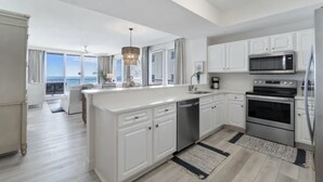 A modern kitchen with white cabinetry, a central island, stainless steel appliances, and a view to the outside.