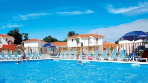 Una piscina con sillas de descanso y sombrillas, rodeada de edificios con techos de tejas rojas.
