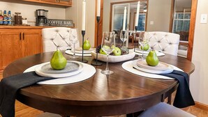 Uma mesa de jantar posta com pratos, copos e peras, com um canto para café e armários ao fundo.