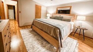Quarto com cama, ventilador de teto, cômoda, mesa de cabeceira e abajur.