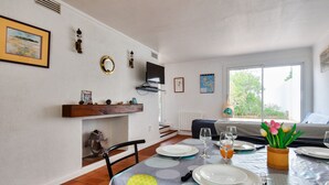 A dining area with a table set for two, a television mounted on the wall, and a window with a view of greenery. - Relaxation and sharing at "Sables d'Or" (La Guérinière)