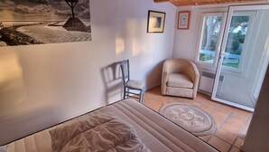 A bedroom with a bed, a chair, a small table, a picture on the wall, and a view of the outside through a door. - Relaxation and sharing at "Sables d'Or" (La Guérinière)