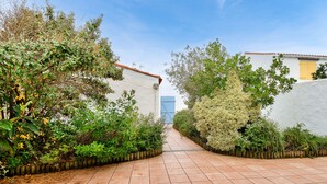 A pathway leading to a building with a blue door, surrounded by lush greenery and white walls. - Relaxation and sharing at "Sables d'Or" (La Guérinière)