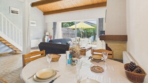 Un coin repas avec une table dressée pour deux personnes, un plafond en bois et une vue sur la terrasse ext érieure.