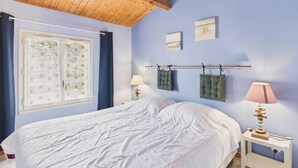 Une chambre avec un plafond en bois, un lit avec une literie blanche, une fenêtre avec des rideaux et deux lampes fixées au mur.
