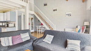 Un salon avec un canapé gris à motifs, un plafond en bois, un escalier et un coin cuisine.