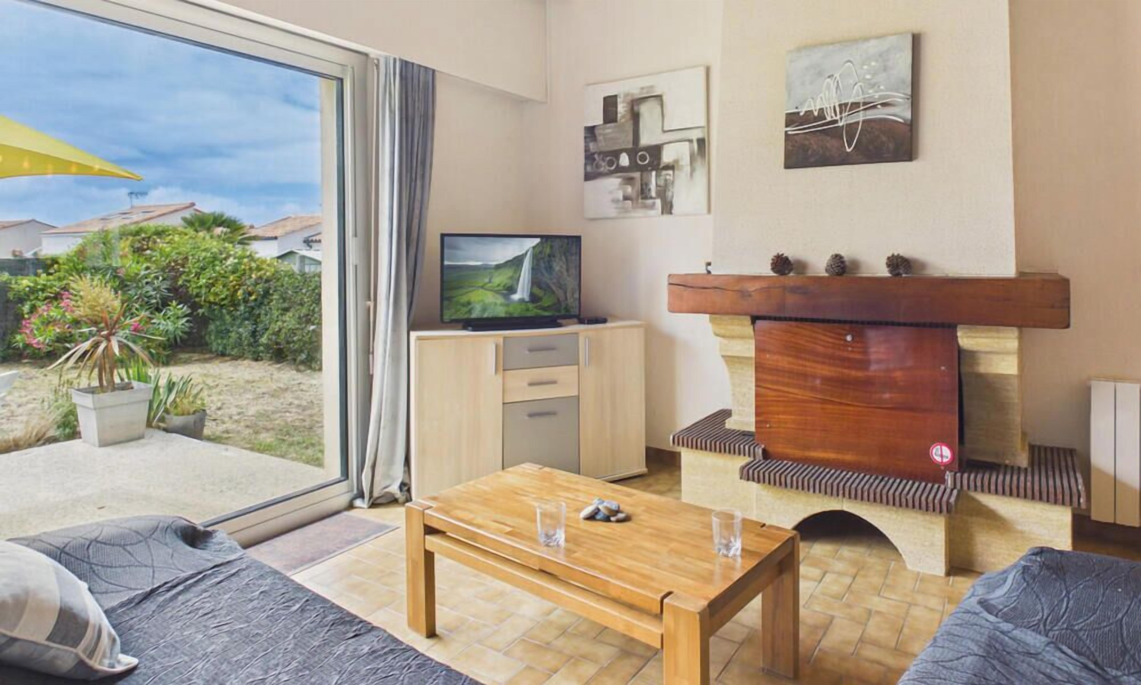 A living room with a TV, sofa, coffee table, fireplace, and a view of the outdoors.