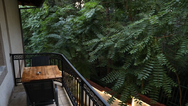 A balcony with a wooden table and chairs, surrounded by a black metal railing.