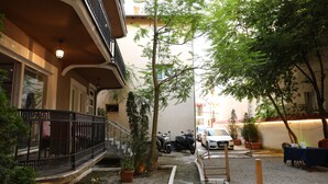 A courtyard with a staircase, potted plants, a scooter, and a car parked in front of a building with a balcony.