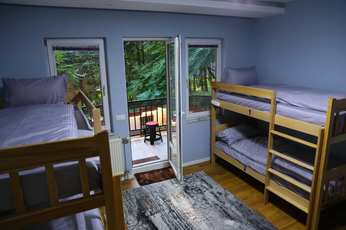 Une chambre de dortoir avec des lits superposés, une tête de lit en bois, un tapis à motifs et une vue sur un balcon avec une balustrade.