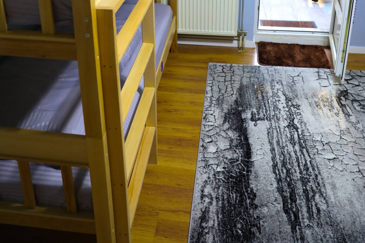Une chambre avec un lit superposé, une fenêtre avec des stores, un radiateur et une vue sur un balcon agrémenté de plantes.