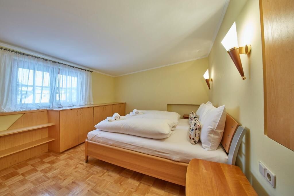 Une chambre à coucher avec un lit en bois, une table de chevet, une fenêtre avec des rideaux légers et des lampes fixées au mur.
