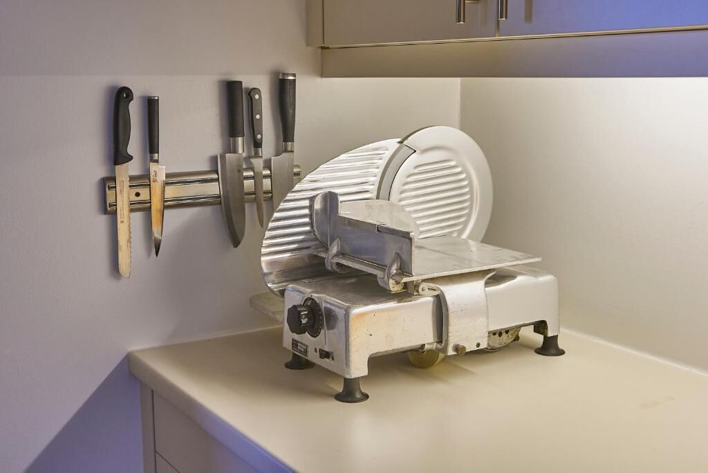 A kitchen with a meat slicer, a knife rack, and a sink.