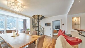 A modern dining area with a wooden table and chairs, a spiral staircase, and a view of the outdoors. - Marys Holiday Penthouse (Saalbach-Hinterglemm)
