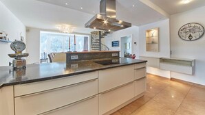 A modern kitchen with a central island, stainless steel range hood, and a large wall clock. - Marys Holiday Penthouse (Saalbach-Hinterglemm)