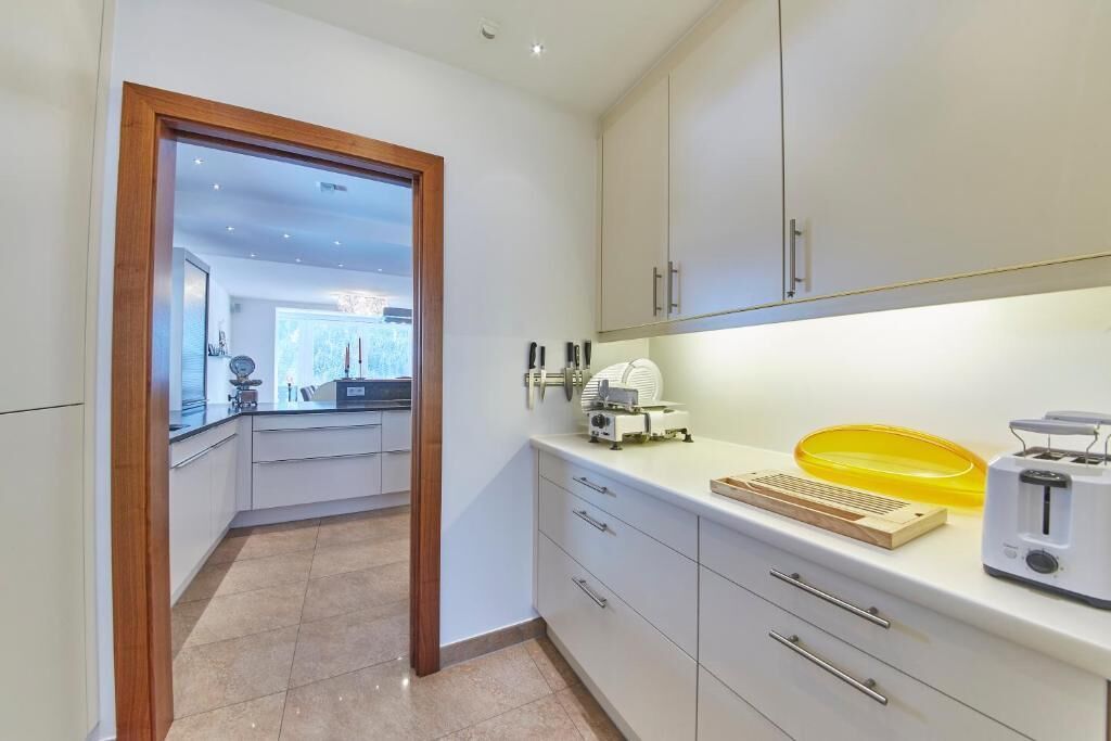 A modern kitchen with white cabinets, a wooden door, and a view into the dining area.