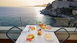 Une table dressée avec des aliments pour le petit-déjeuner, offrant une vue pittoresque sur la mer et un bâtiment historique.