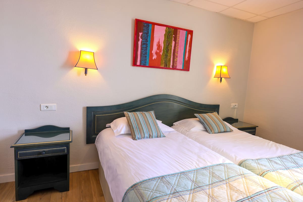 Un lit double avec deux tables de chevet, chacune équipée d’une lampe, dans une pièce dont le mur est uni et qui est éclairée par un luminaire au plafond.