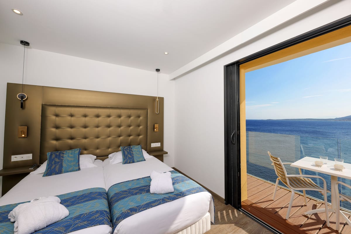 Une chambre d’hôtel avec un grand lit, une vue sur la mer et un balcon équipé d’une table et de chaises.