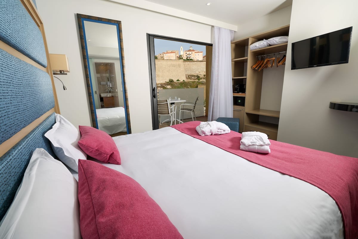 Une chambre d’hôtel avec un lit, une télévision, une armoire et un balcon donnant sur des immeubles.