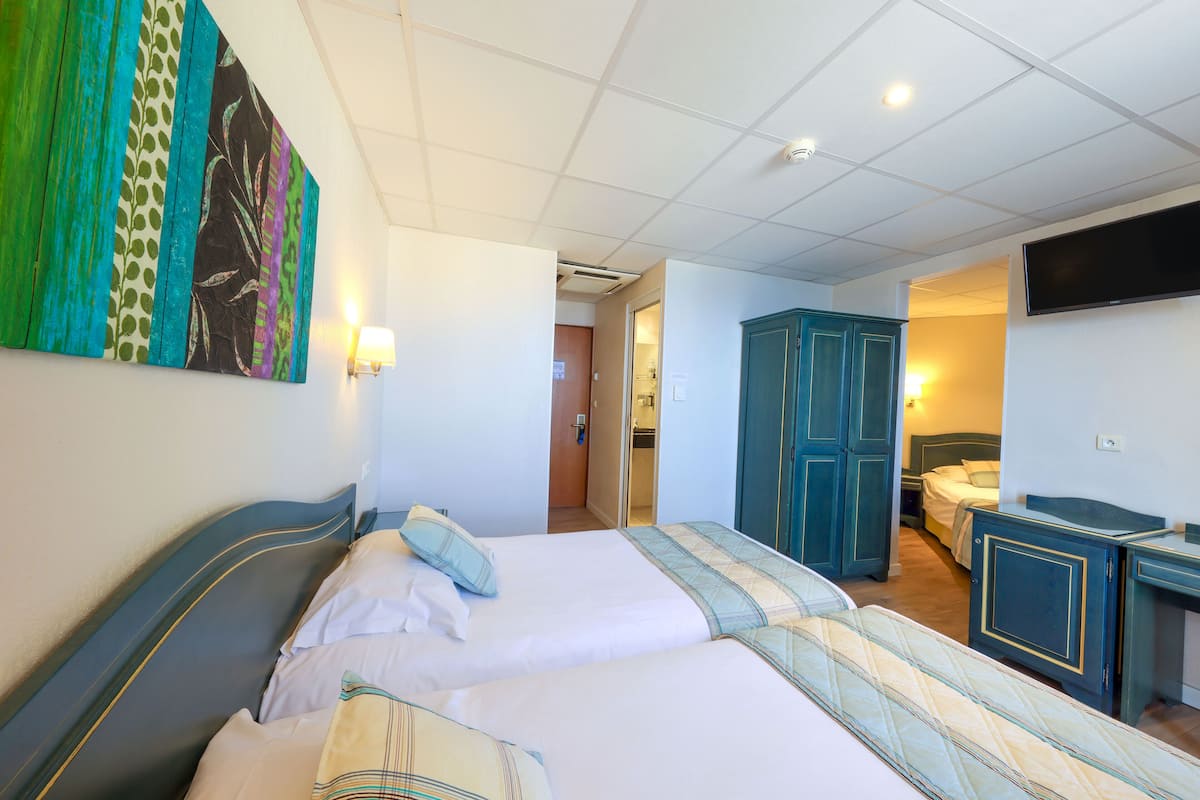 Une chambre d’hôtel avec deux lits, une télévision, une armoire et une salle de bain visible à travers une porte ouverte.