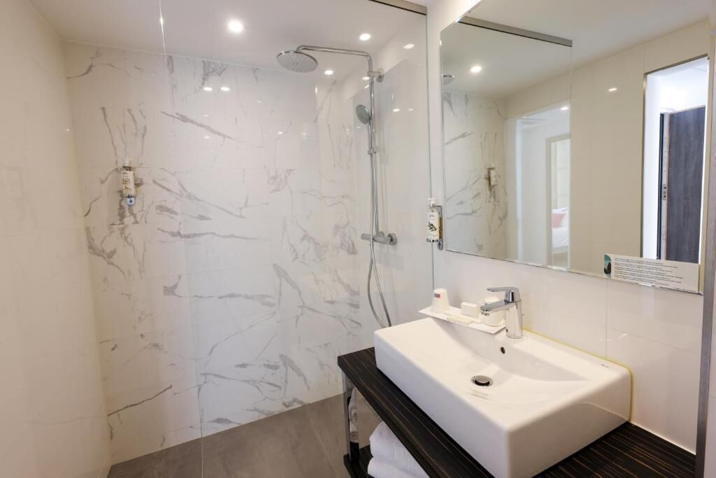 Une salle de bain moderne avec un mur de douche en marbre, un lavabo blanc et un grand miroir.