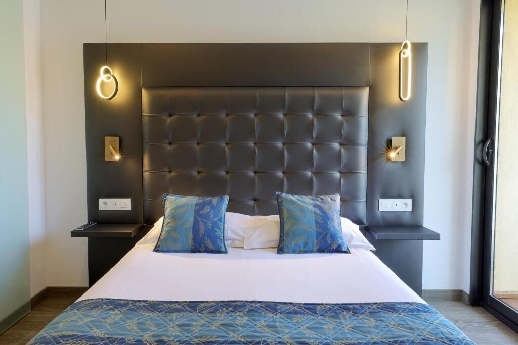 Une chambre à coucher moderne avec une tête de lit capitonnée, deux tables de chevet et un grand lit recouvert d’une literie à motifs.