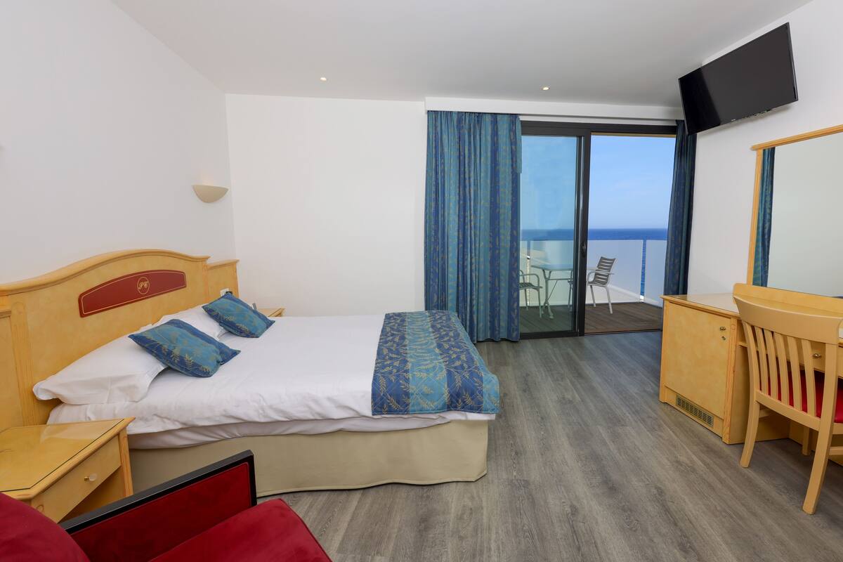 Une chambre d’hôtel avec un lit, un bureau, une chaise, une télévision et un balcon avec vue.