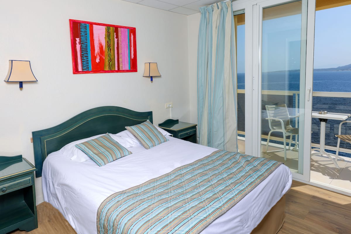 Une chambre d’hôtel avec un lit, deux tables de chevet, une fenêtre avec des rideaux et une vue sur la mer.