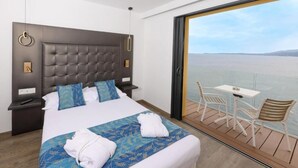 Une chambre d’hôtel moderne dotée d’un grand lit, offrant une vue sur la mer et disposant d’un balcon avec coin salon extérieur.