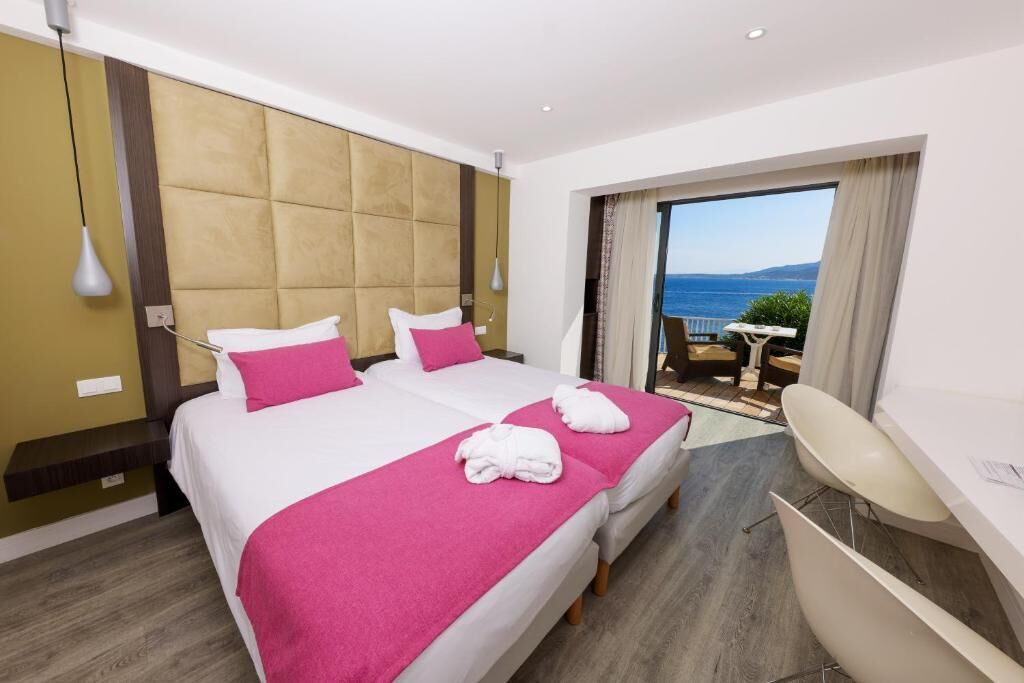 A hotel room with two beds, a desk, and a view of the sea.