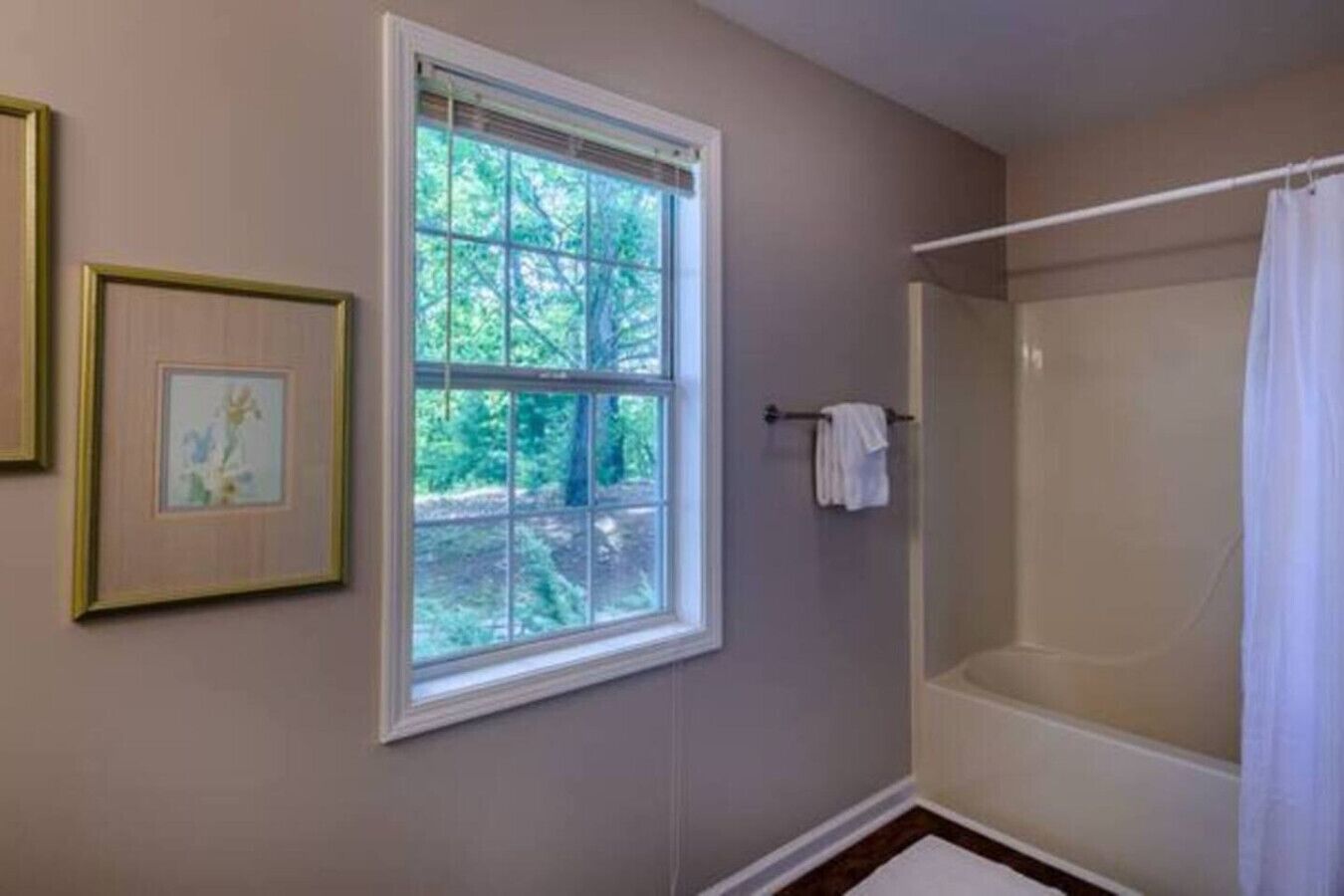 A bathroom with a window, a shower, and framed artwork on the wall.