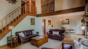 A spacious living room with a staircase, leather sofas, a wooden coffee table, and a dining area with chairs and a table. - Rosewood Cottage Tucked Away in the Mountains (Franklin)