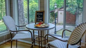 A cozy seating area with wicker chairs and a round table, a sign reading "Welcome to Rosewood Cottage," and a view of a lush garden through large windows. - Rosewood Cottage Tucked Away in the Mountains (Franklin)