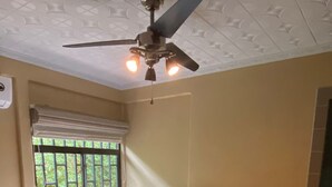 A bedroom with a bed, a nightstand, a ceiling fan, and a window with bars. - 2 Room Family Home in Bahia, Gated, walking distance to National Park (Bahia Ballena)