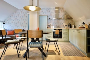 A cozy kitchen with a dining area, featuring a round table, chairs, and a hanging light fixture.