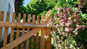 A wooden gate with a metal latch, surrounded by lush greenery and flowering plants.