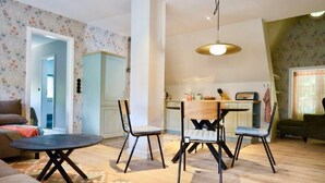 A living room with a round coffee table, two chairs, and a sofa. There is a kitchen in the background with a dining table and chairs.