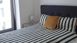 Habitación de hotel con una cama, ropa de cama a rayas, un cabecero tapizado oscuro y una sola almohada marrón.