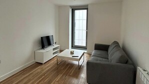 Una sala de estar moderna con un televisor de pantalla plana sobre un mueble blanco, un sofá gris y una pequeña mesa de centro.
