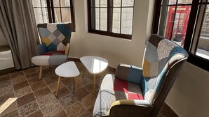A cozy living room with patterned sofas, a small white table, and large windows with a view of a brick wall and a red telephone booth. - 1 Antica jabalal-lwebdeh (Amman)