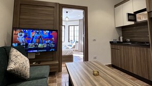 A modern living room with a flat-screen TV, a green sofa, a wooden dining table, and a kitchen area with wooden cabinets and a microwave. - 1 Antica jabalal-lwebdeh (Amman)